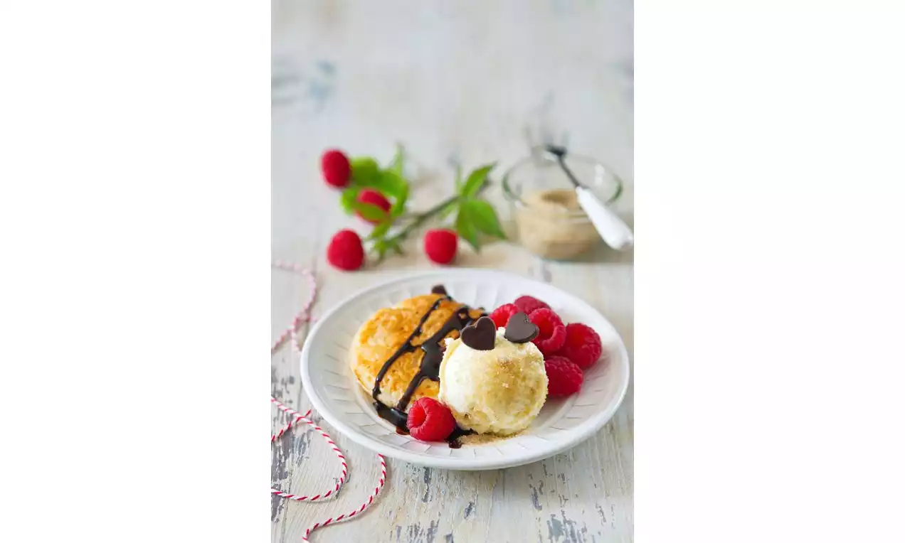 Zlato rjavi sladoledni kolački nežne teksture, preliti s temno čokolado in obkroženi s svežimi malinami na belem krožniku