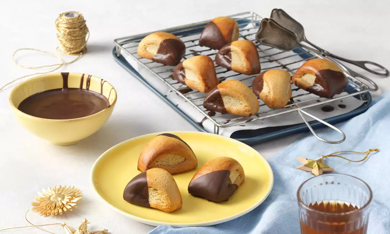 St. Galler Biberle mit goldbrauner, glatter Oberfläche, teils in dunkle Schokolade getaucht, auf gelbem Teller und Gitter angerichtet