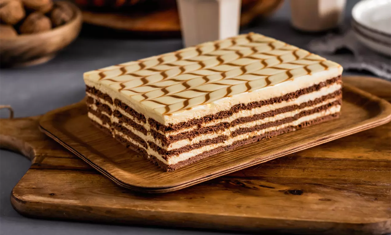 Правоъгълна торта с редуващи се слоеве шоколадови бисквити и гладък баварски крем, покрита с карамелени линии върху дървена подложка