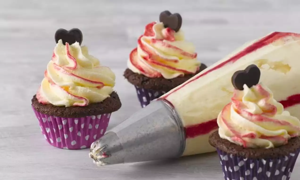 Minicupcakes de chocolate com cobertura cremosa branca e vermelha em espiral, decorados com corações de chocolate, sobre forminhas roxas com bolinhas