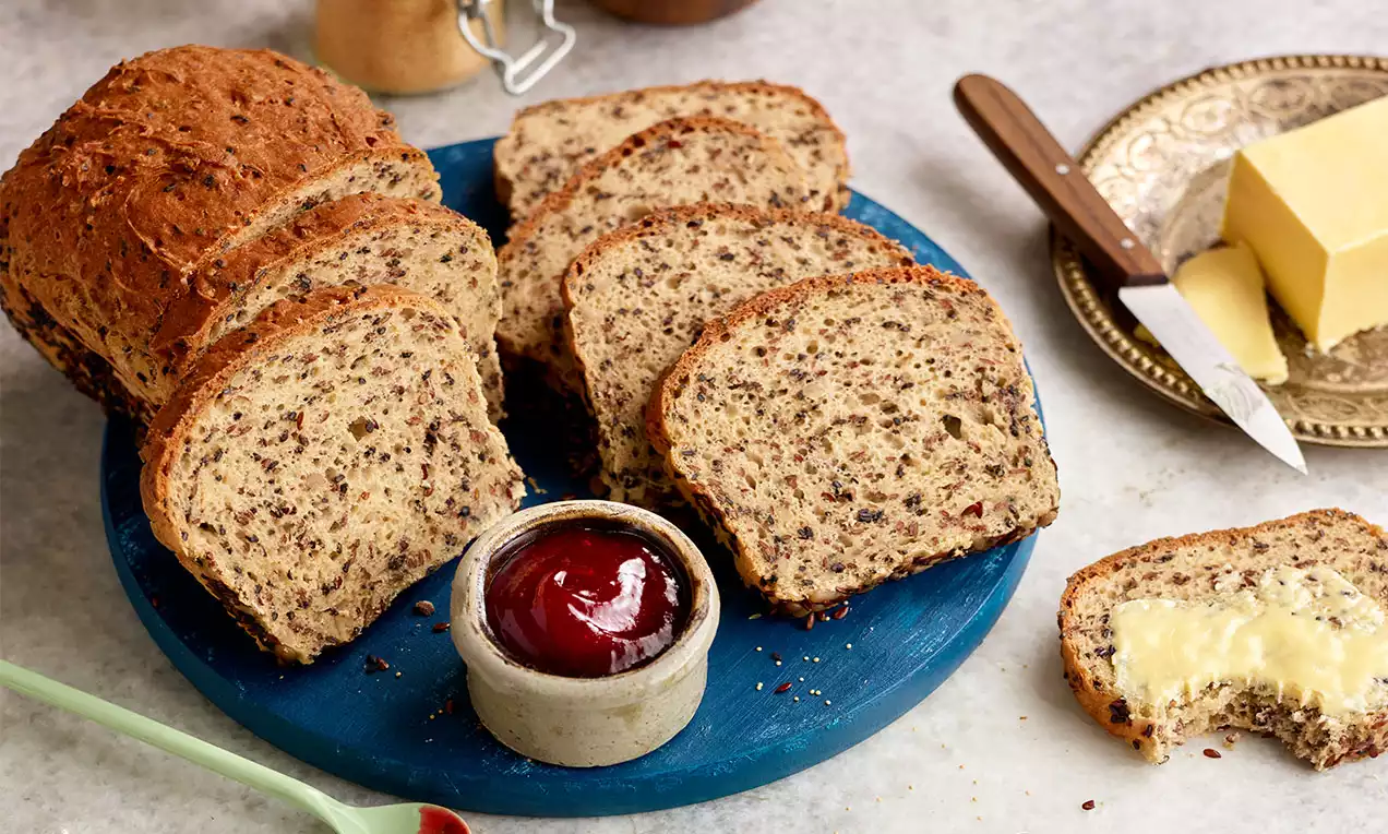 Amaranth-Brot in dicke Scheiben geschnitten, goldbraune Kruste und körnige Textur, arrangiert auf einem blauen Teller neben Butter und Marmelade