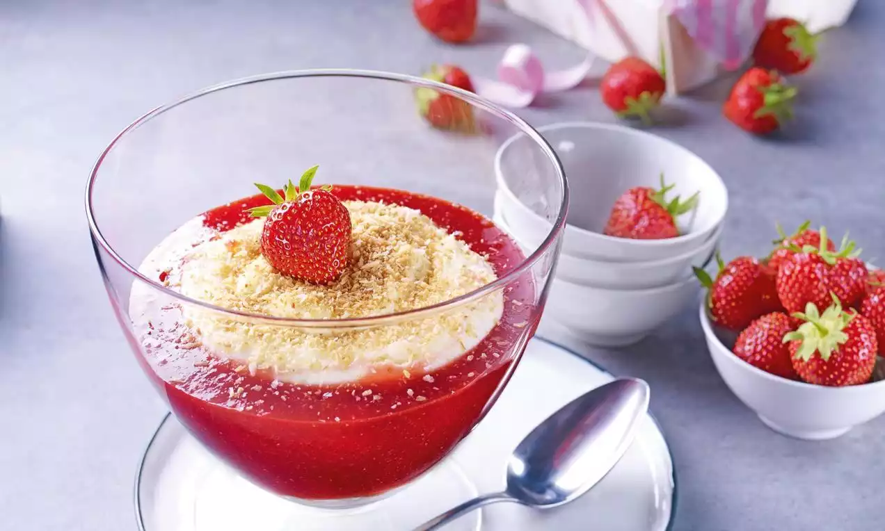 Sobremesa cremosa com camada vermelha brilhante de purê de morango, coberta com creme branco suave, farofa fina e morango inteiro no centro