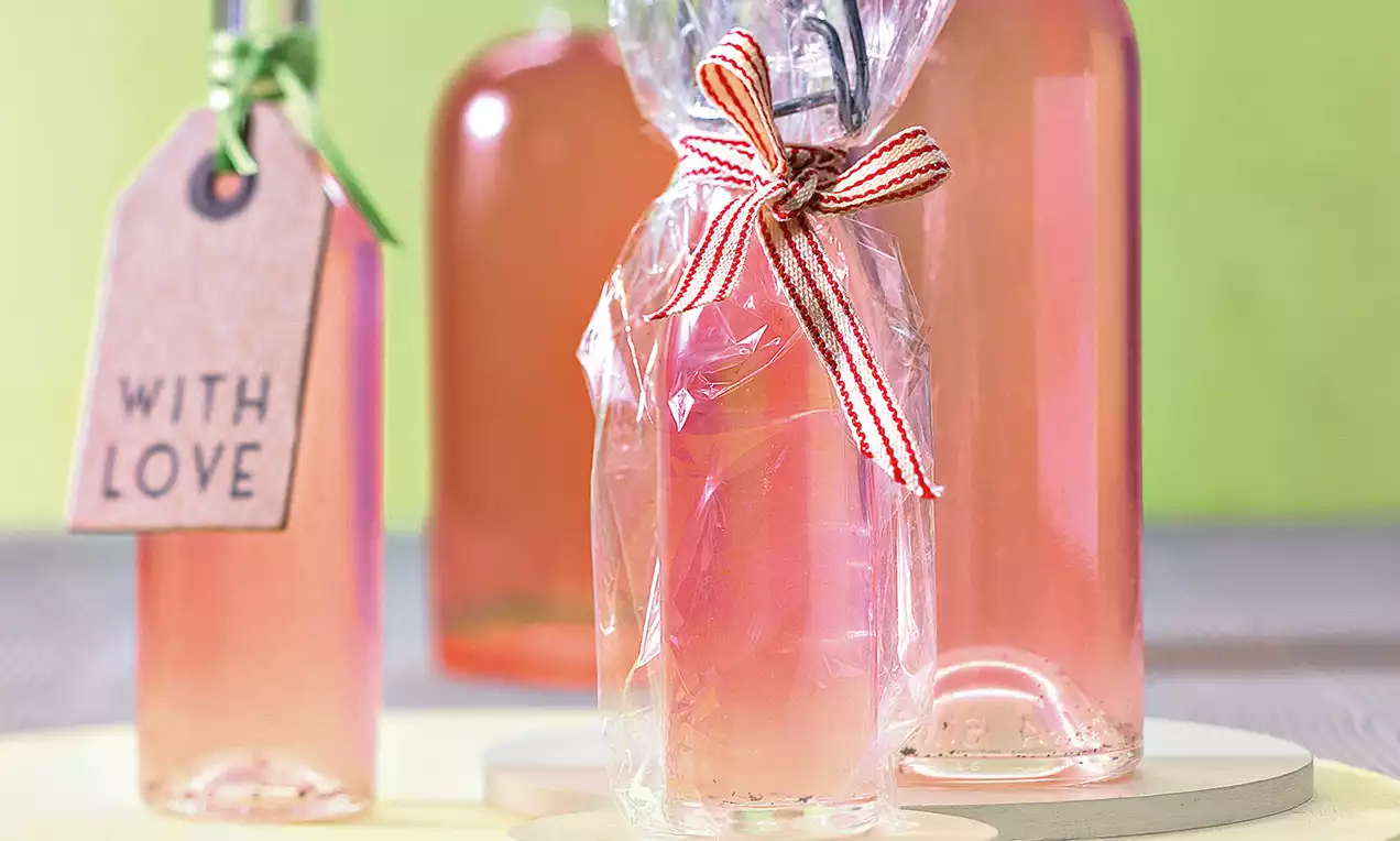 Bouteilles de liqueur rose pastel, aux reflets translucides et brillant, emballées avec du ruban rayé rouge sur un fond vert lime