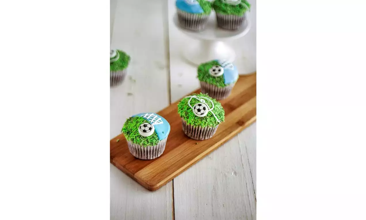 Cupcakes med grønt og blått glasur som fotballbane, pyntet med små svarte og hvite fotballer på en avlang trefarget serveringsplate