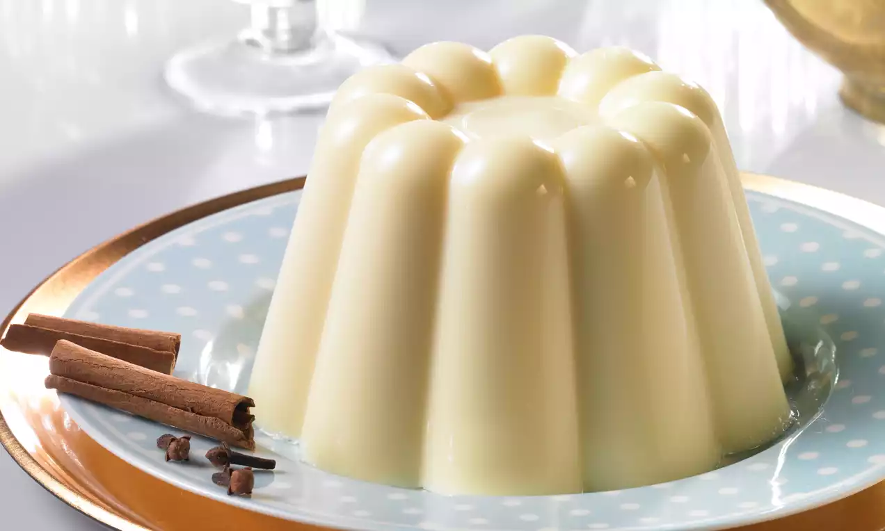 Flan vanille lisse et crémeux, en forme de couronne pâle, posé sur une assiette blanche bordée d'or avec bâtons de cannelle