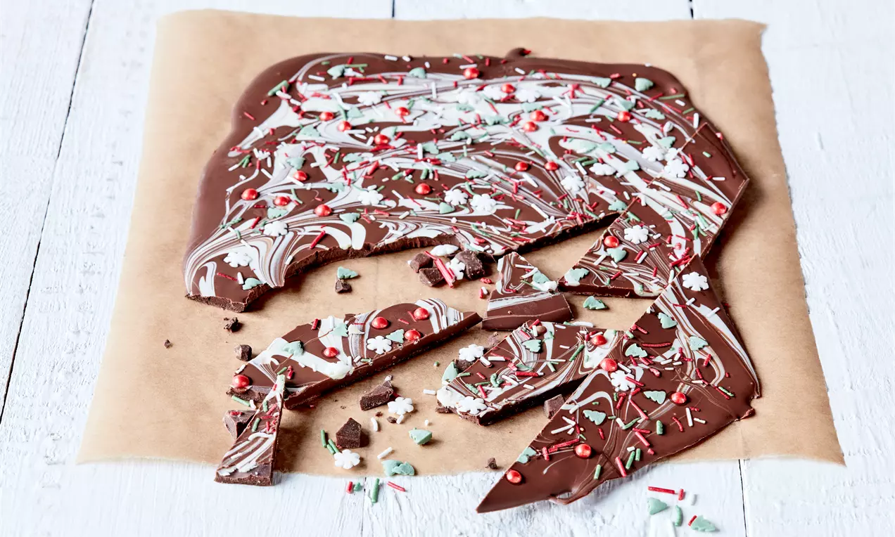 Разтопен тъмен шоколад, оформен в неравни платки с мраморен десен от бял шоколад и цветни захарни пръчици върху кафява хартия