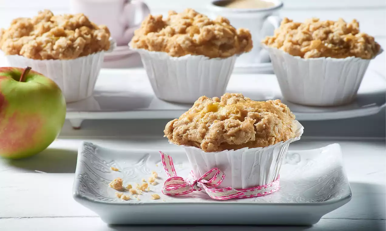 Kullanruskea, rouheapintainen muffinssi valkoisessa paperivuoassa, koristeltu vaaleanpunaisella nauhalla, aseteltuna kuvioidulle lautaselle