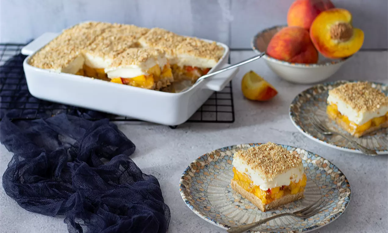 Сладкиш с праскови с правоъгълни парчета с пластове от златисто бисквитено дъно, сочни праскови, крем и хрупкава поръска върху сиво-мраморни чинии