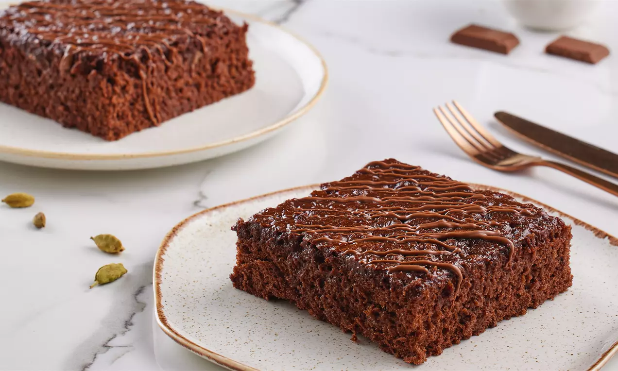 Kakuleli ıslak kek, kare dilimlenmiş, yoğun dokulu, üzerine çikolata sosu gezdirilmiş, beyaz seramik tabakta sunulmuş