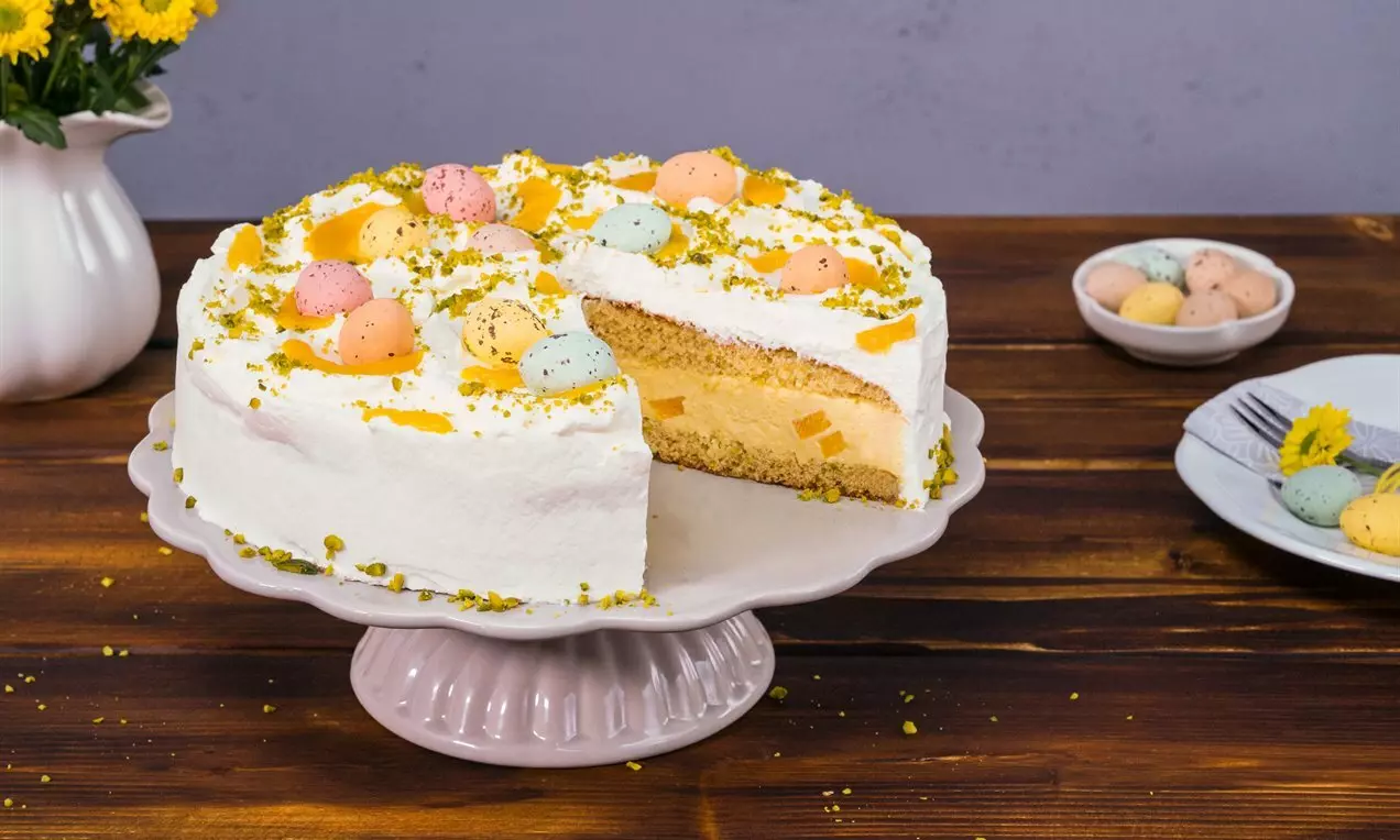 Бяла торта с пухкав крем, шарени шоколадови яйца, ред лимонов мус и поръски от шамфъстък върху изчистена стойка