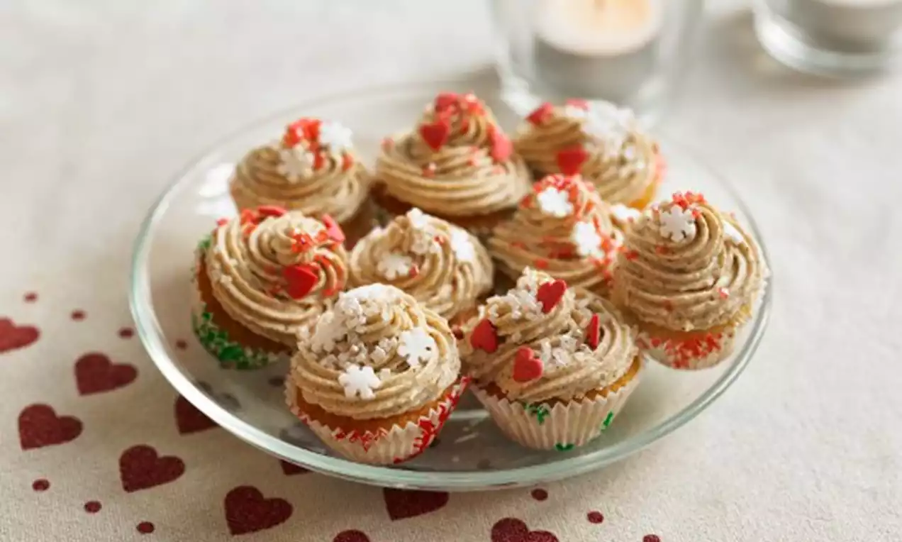 Små cupcakes med krämig spritsad frosting i beige, dekorerade med vita och röda strösselhjärtan och stjärnor på glasfat, ljus och hjärtdetaljer