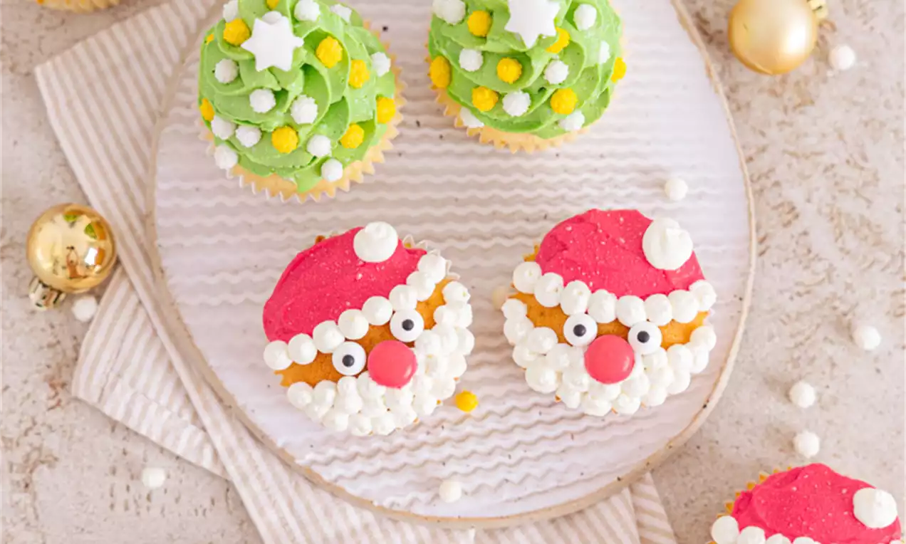 Praznični kolački z rdečimi klobuki, bradami iz bele kreme in očmi iz sladkornih perl ter zeleni smrečicami s posutimi zvezdami in kroglicami na belem krožniku