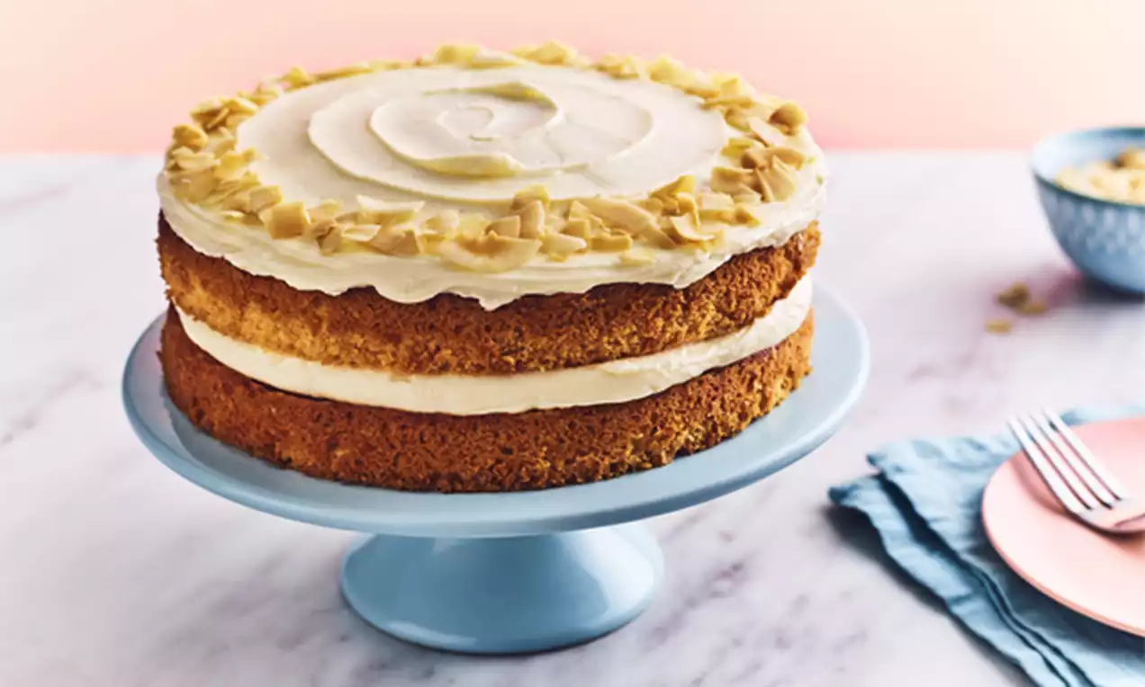 A two-layer coconut cake with golden sponge, creamy white frosting, and toasted coconut flakes on a light blue cake stand
