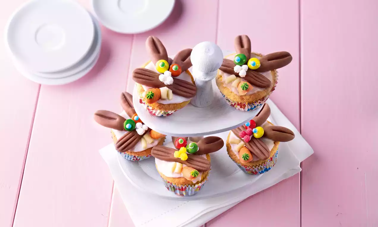Muffins moelleux décorés d’oreilles en chocolat brun, fleurs en sucre colorées et posés sur un plateau blanc à deux étages