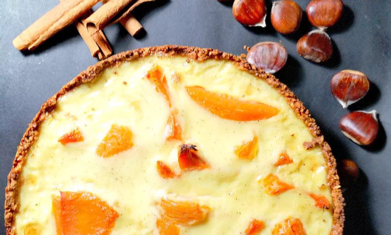Тиквен тарт с хрупкав ръб, кремообразен жълт пълнеж и топли оранжеви парченца тиква, върху тъмен фон с кестени и канелени пръчици