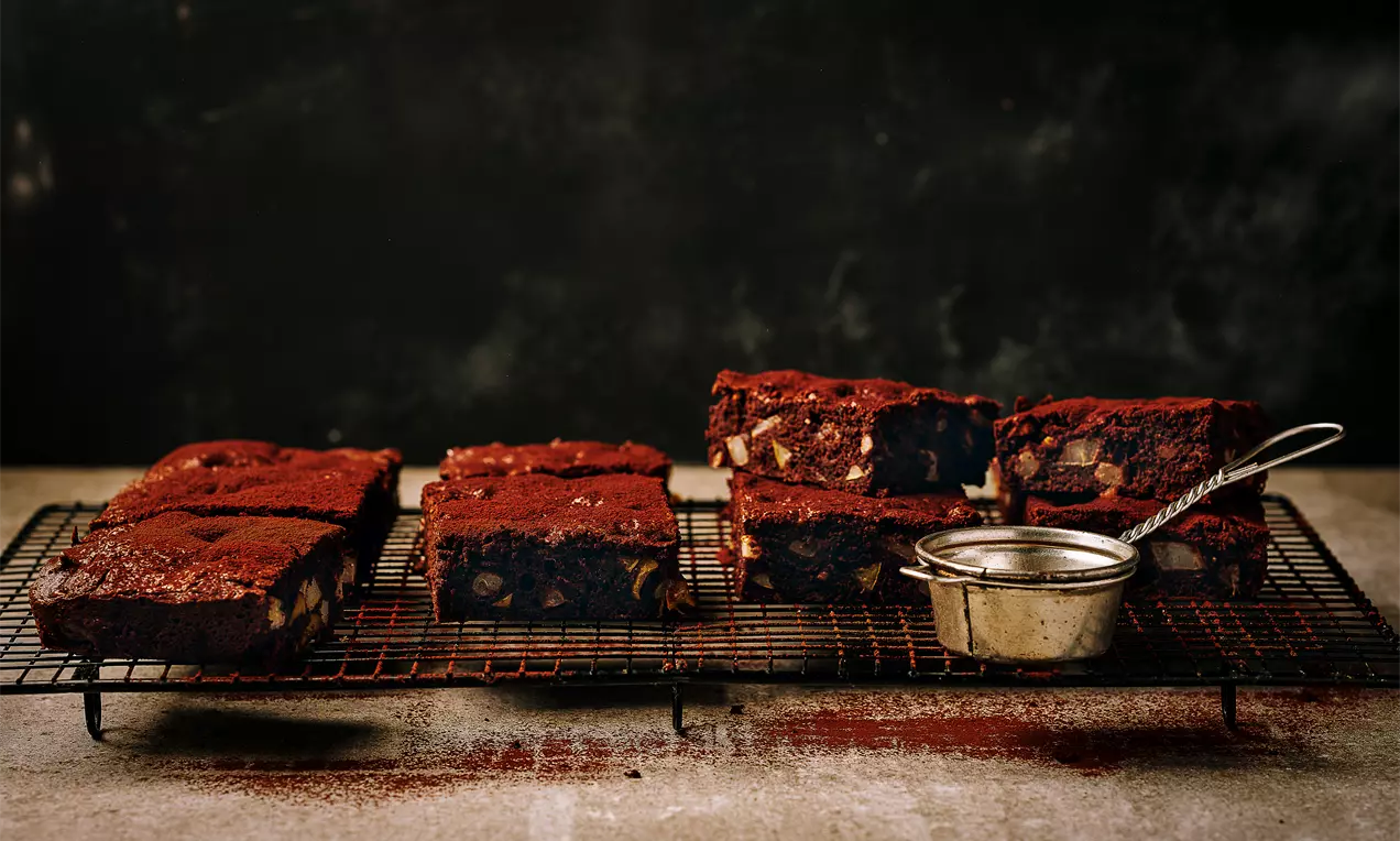 Ректангуларни парчета дълбококафяво брауни с втъкани светли парчета круша върху метална решетка, леко поръсени с какао