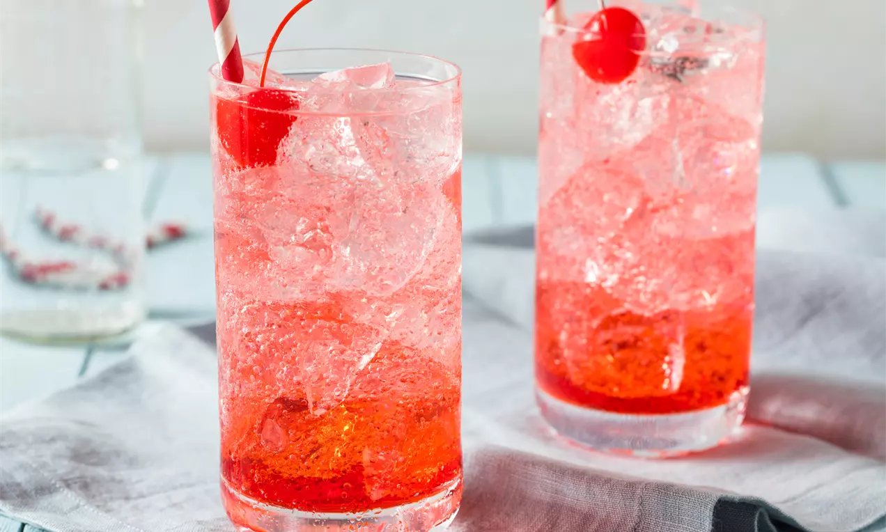Два високи стъклени чаши с розово ледено фрозе, яркочервени череши и хартиени сламки на светлосиня текстилна салфетка