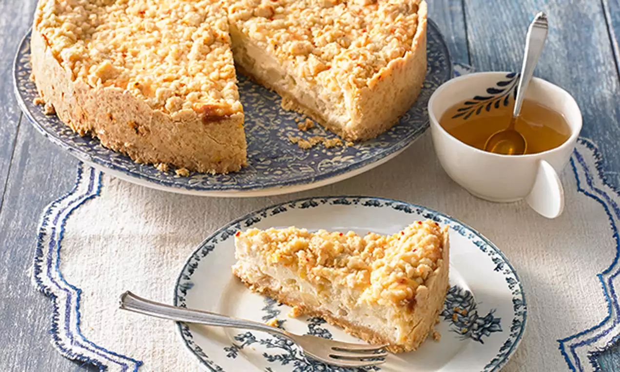 Ein Stück Zitronen-Chili-Streuselkuchen mit goldbrauner Kruste, Streuseln und cremiger Füllung auf floralem Teller neben Tasse mit Honiglöffel