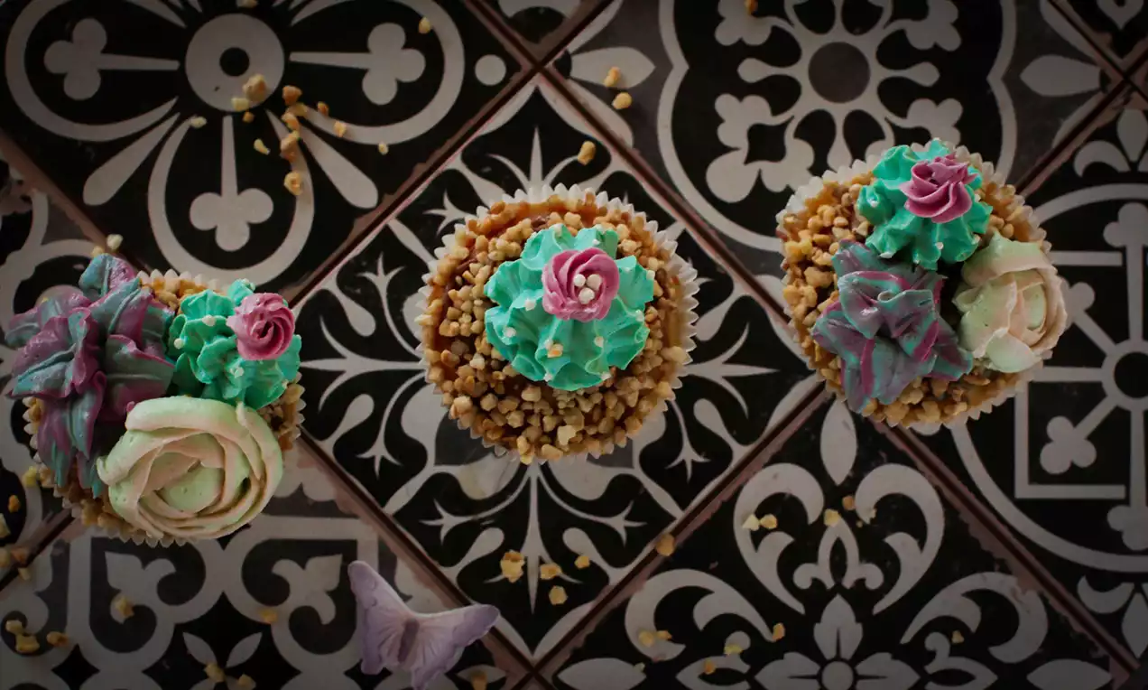 Mit grünem, rosafarbenem und lilafarbenem Zuckerguss verzierte Cupcakes auf einem geometrischen Fliesenmuster mit goldenen Streuseln