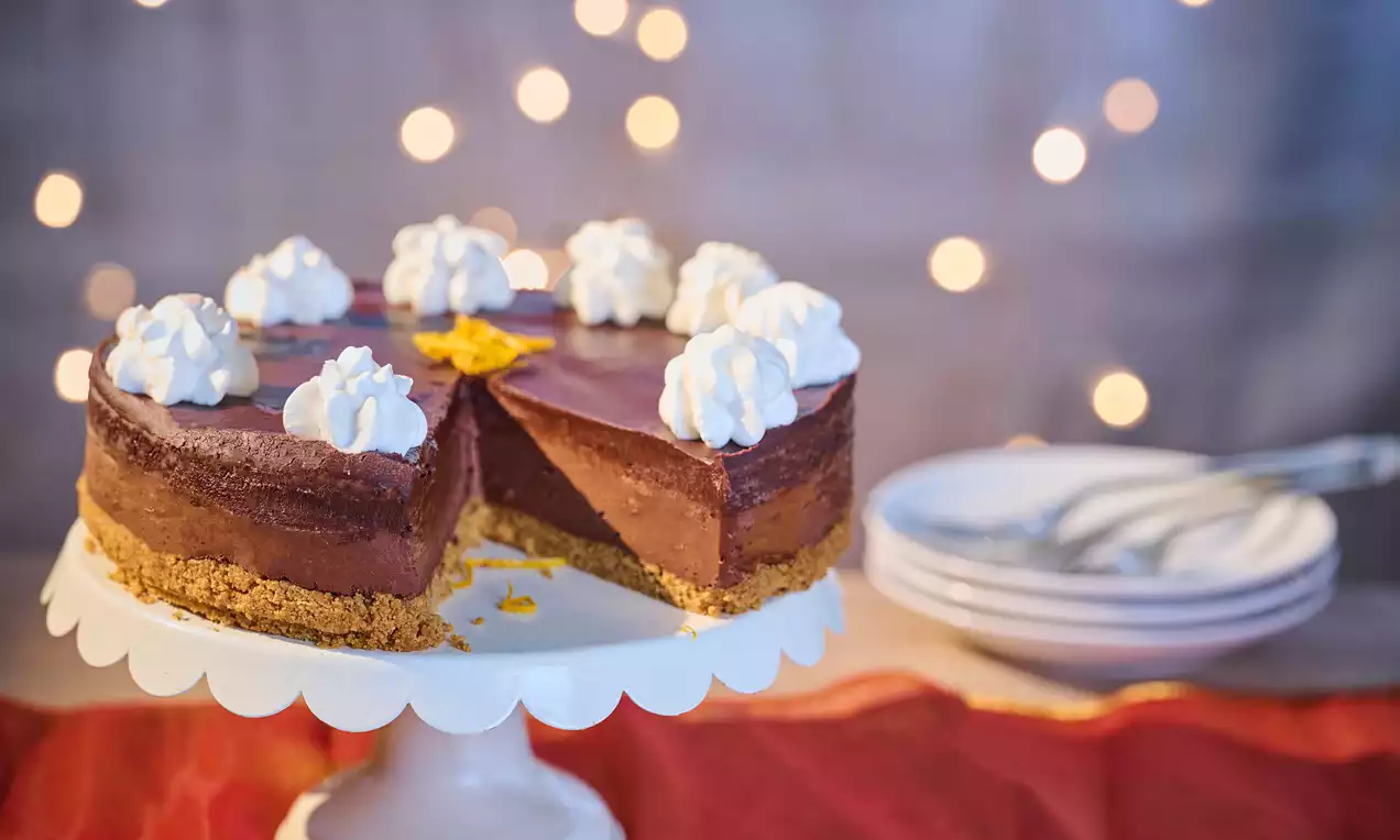 Vegan chocolate orange cheesecake with rich brown filling on a crumbly biscuit base, topped with whipped swirls and orange zest