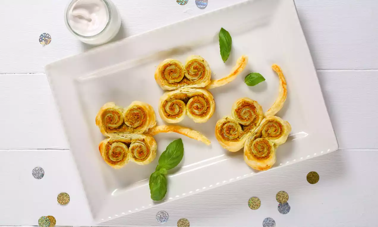 Aranybarna, csiga formájú, leveles tészta lóherék zöldes töltelékkel, hosszúkás szárakkal, fehér téglalap alakú tányéron bazsalikomlevéllel díszítve