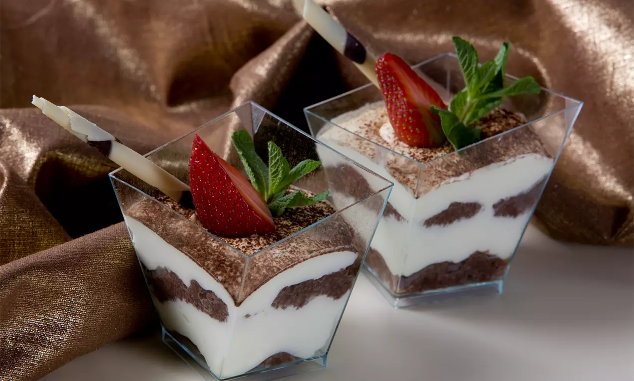 Elegantní sklenky s vrstveným tiramisu, střídající světlý krém a tmavou piškotovou vrstvu, ozdobené jahodami, mátou a čokoládovými tyčinkami