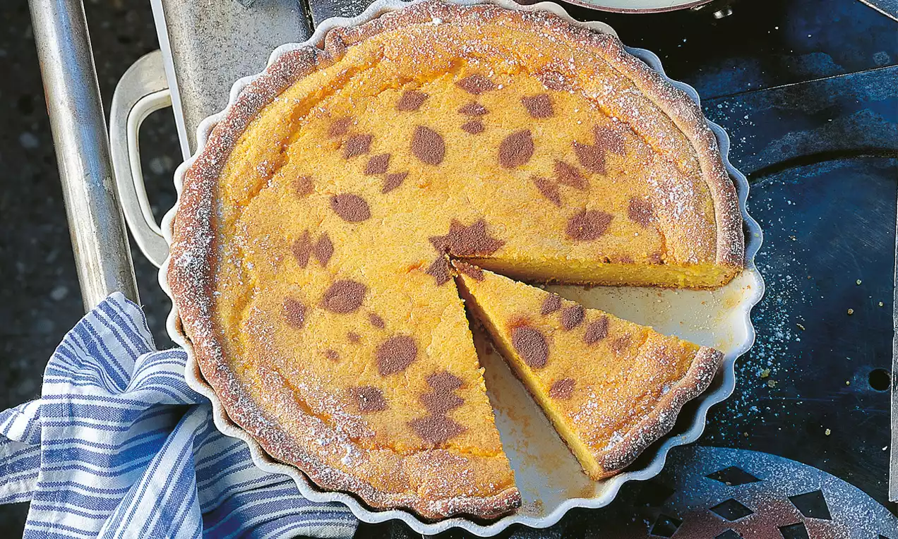 Goldgelber Polenta-Kuchen mit braunem Muster in einer weißen gewellten Form, angeschnitten und dekorativ angerichtet mit einem Stofftuch