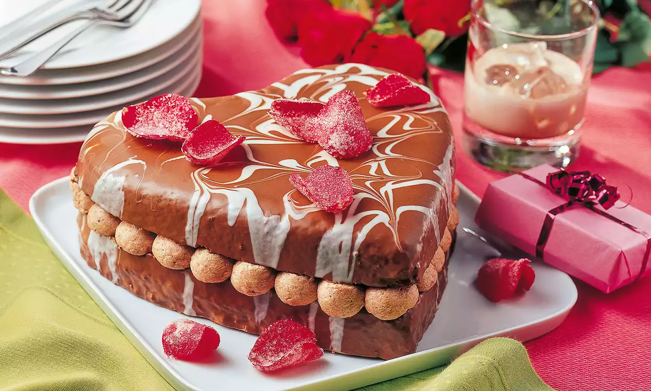 Gâteau en forme de cœur avec un glaçage marbré caramel et blanc, bordé de choux et décoré de pétales de sucre rouges