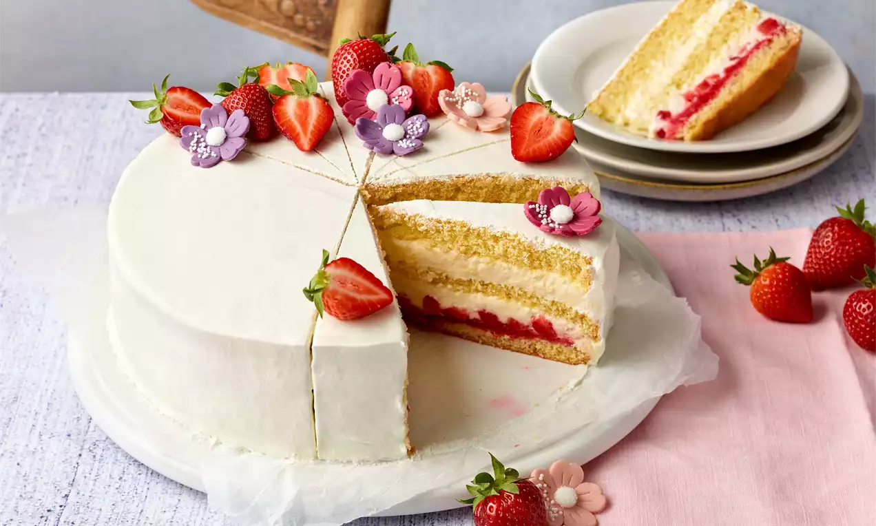 Jemná biela torta na podnose so zdobením z čerstvých jahôd a cukrových kvietkov, vnútro vrstvené krémom a jahodovým pudingom