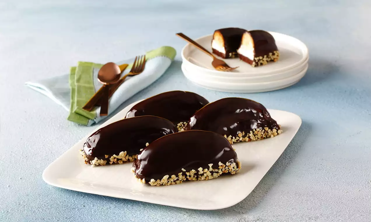 Parlak çikolata kaplı, yarım ay şeklinde, kenarları ince kıyılmış fındıklarla kaplanmış puding dolgulu tatlılar beyaz tabakta sunulmuş