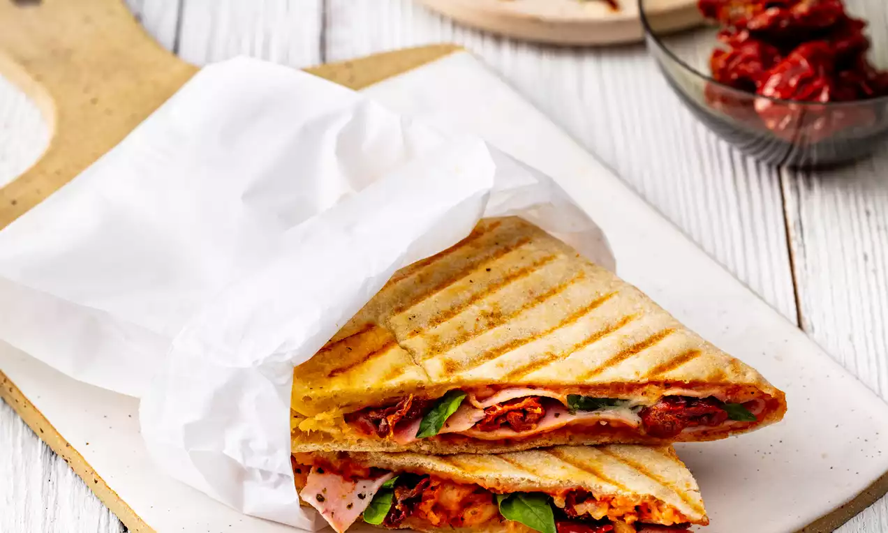 Knusprig gegrilltes Pizza-Sandwich mit goldbraunen Grillstreifen, gefüllt mit rotem Tomatenbelag, Basilikum und Schinken, auf Holzbrett serviert