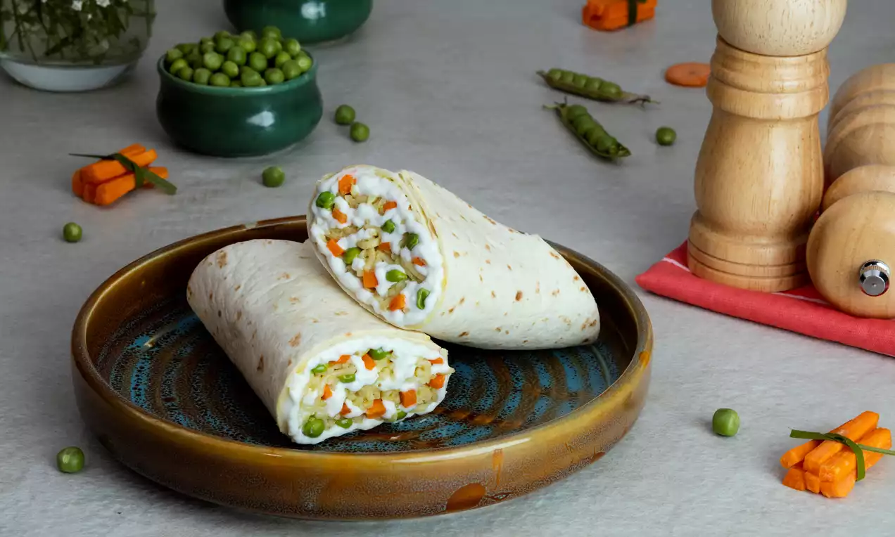 Soft tortilla wraps neatly folded and sliced to reveal a colorful filling of vibrant orange carrots, green peas, and creamy white sauce on a glazed blue plate
