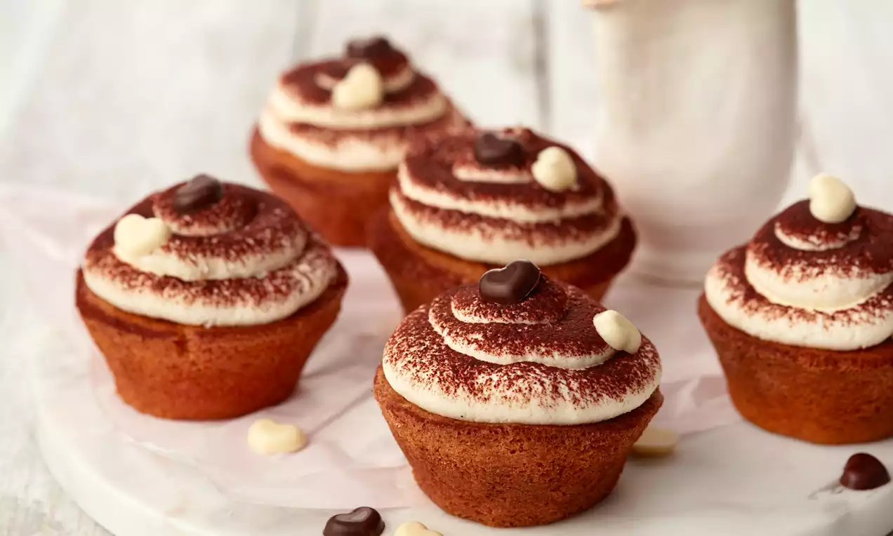 Tiramisu-Cupcakes mit goldbraunem Teig und cremigen, kakaobestäubten Sahnetupfen, garniert mit dunkler und weißer Schokolade auf weißer Platte