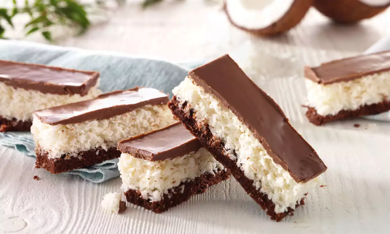 Coconut chocolate bars with a rich brown base, fluffy white coconut layer, and glossy chocolate topping arranged on a blue napkin