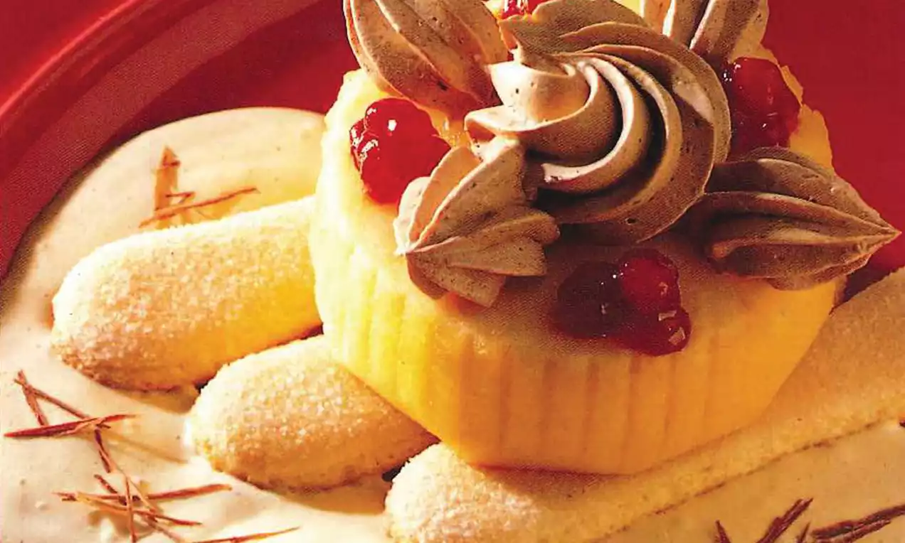 Entremets jaune clair aux bords cannelés, décoré de crème chocolatée joliment dressée et de fruits rouges sur une sauce vanillée blanche