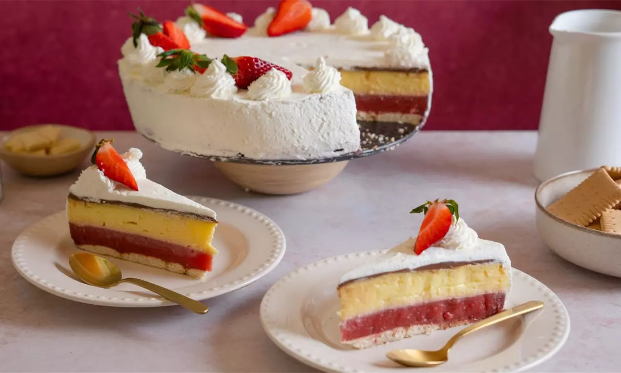 Kapri torta sa slojevima svetložutog krema, crvenog želea i tamne čokolade, ukrašena belim šlagom i svežim jagodama na tanjiru