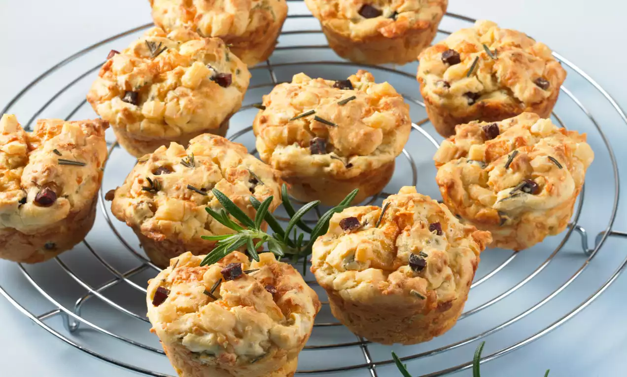 Goldbraune Parmesan-Muffins mit knuspriger Oberfläche und Rosmarinspitzen, auf einem silbernen Gitter mit frischen Rosmarinzweigen angerichtet