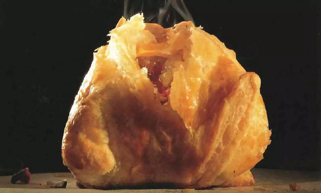 Goudbruin bladerdeeg, opengebroken aan de bovenkant, onthult gestoomde appelvulling op een donkere ondergrond