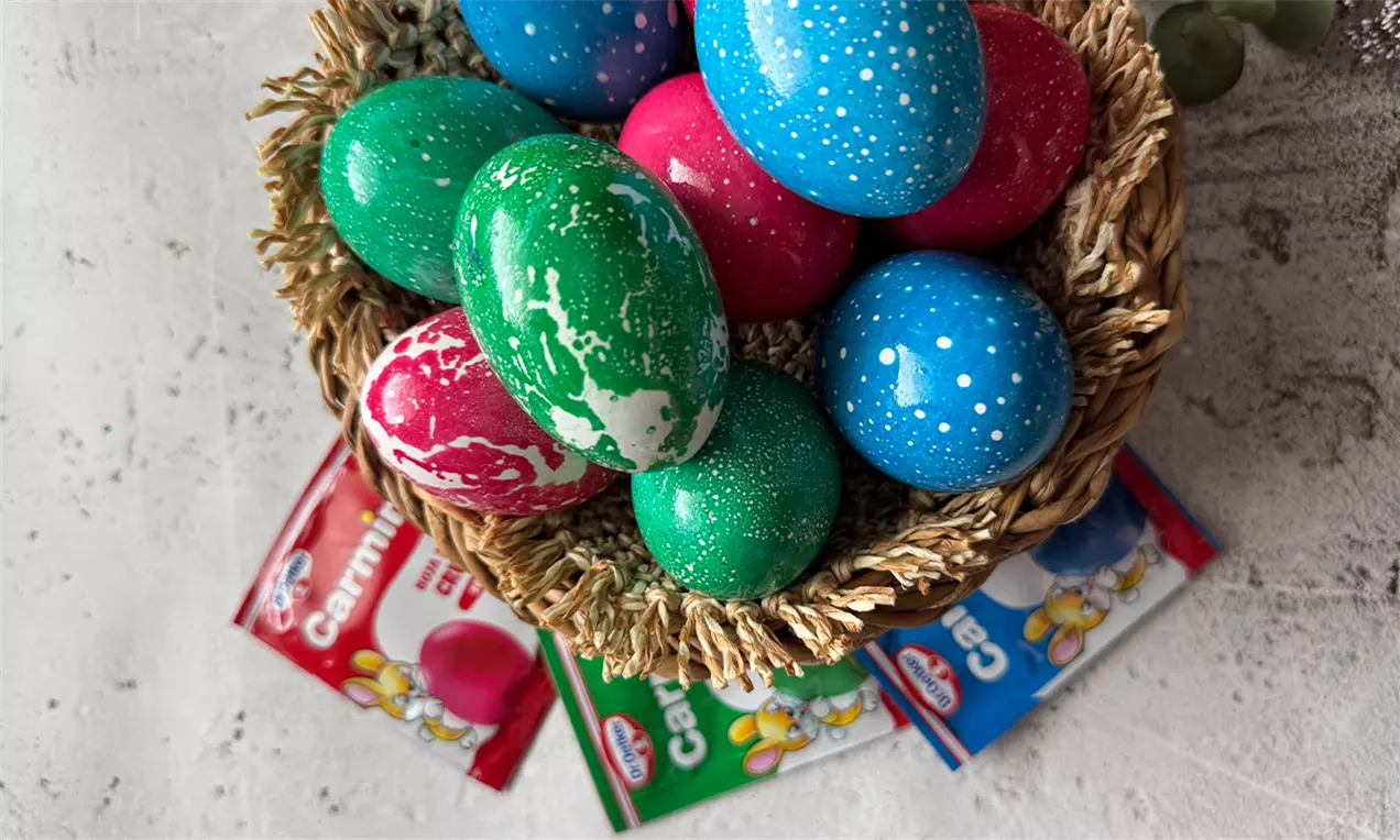 Šarena jaja u plavoj, zelenoj, crvenoj i beloj boji s uljanim efektom raspoređena u pletenoj korpi na svetloj podlozi