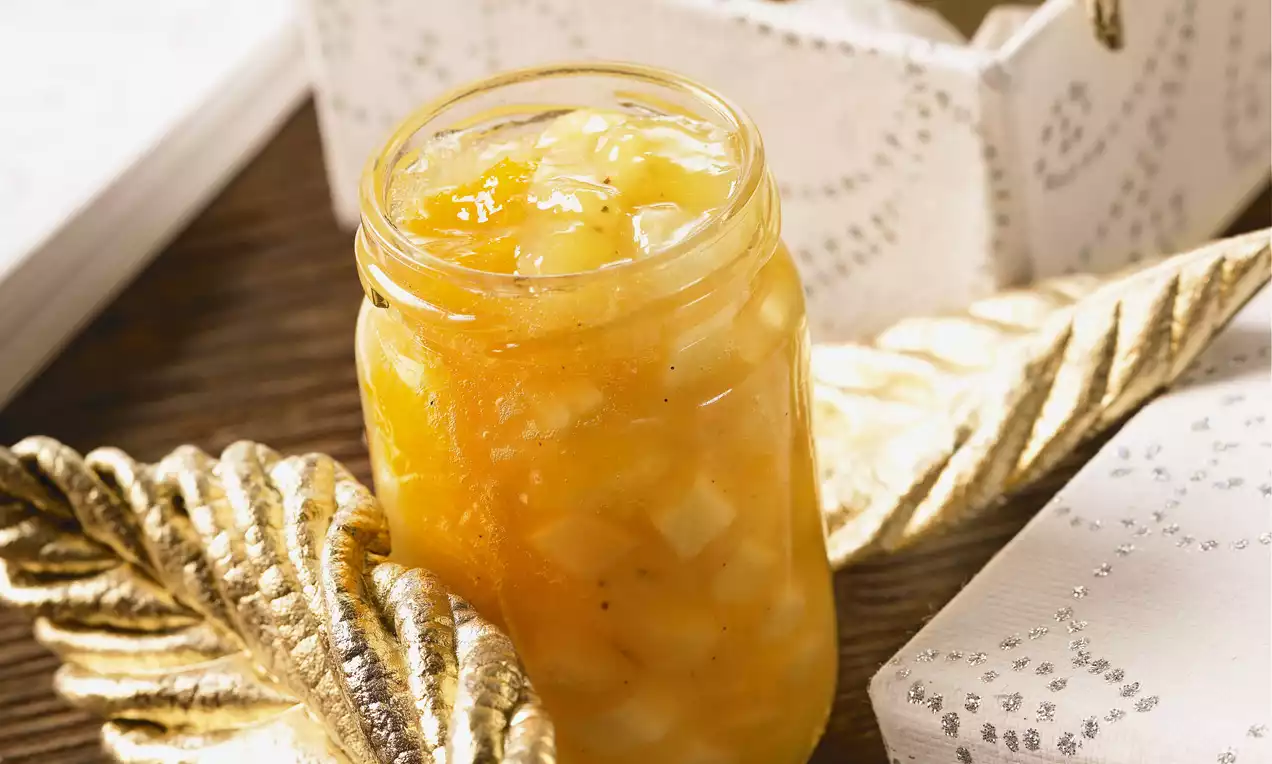 Confiture dorée à la texture lumineuse avec morceaux de fruits translucides dans un pot en verre entouré de feuilles dorées et d’un papier festif