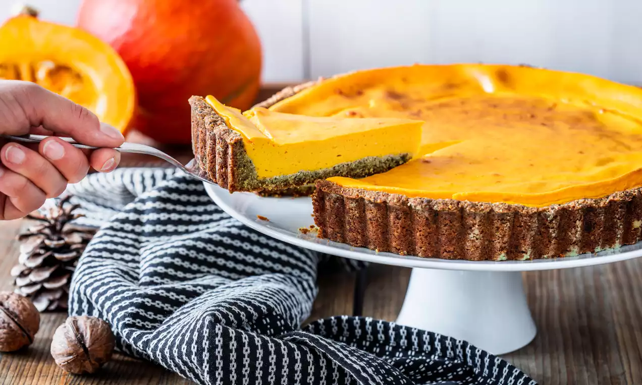 Glutenfri pumpapaj med gyllenoransje glatt fyll i en mørk brun paiskall, servert på et hvitt fat med lintekstur duk og høstdekorasjoner