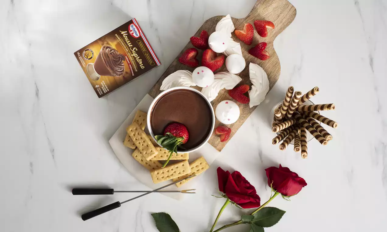 Rich chocolate mousse in a round bowl, surrounded by strawberries, meringue kisses, biscuit sticks, and shortbread on a wooden board