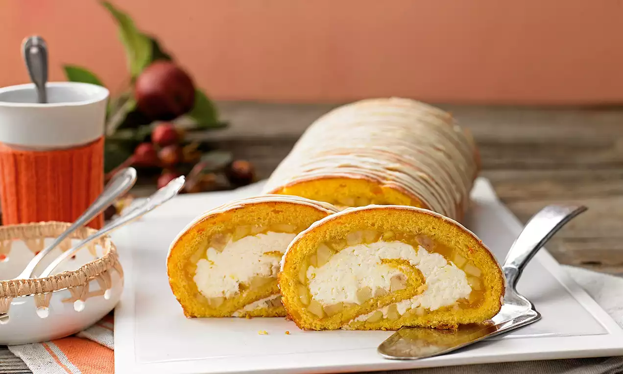 Rolada tople narandžaste boje, spiralno uvijena, sa slojevima filaste bijele kreme, poslužena na bijelom tanjiru uz metalni nož