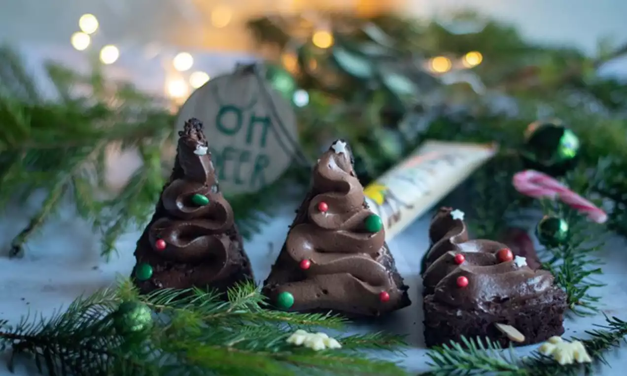 Schokoladen-Brownies in Tannenbaumform mit geschwungenem Schokofrosting, bunten Perlen und Dekoration aus grünen Tannenzweigen und Lichtern