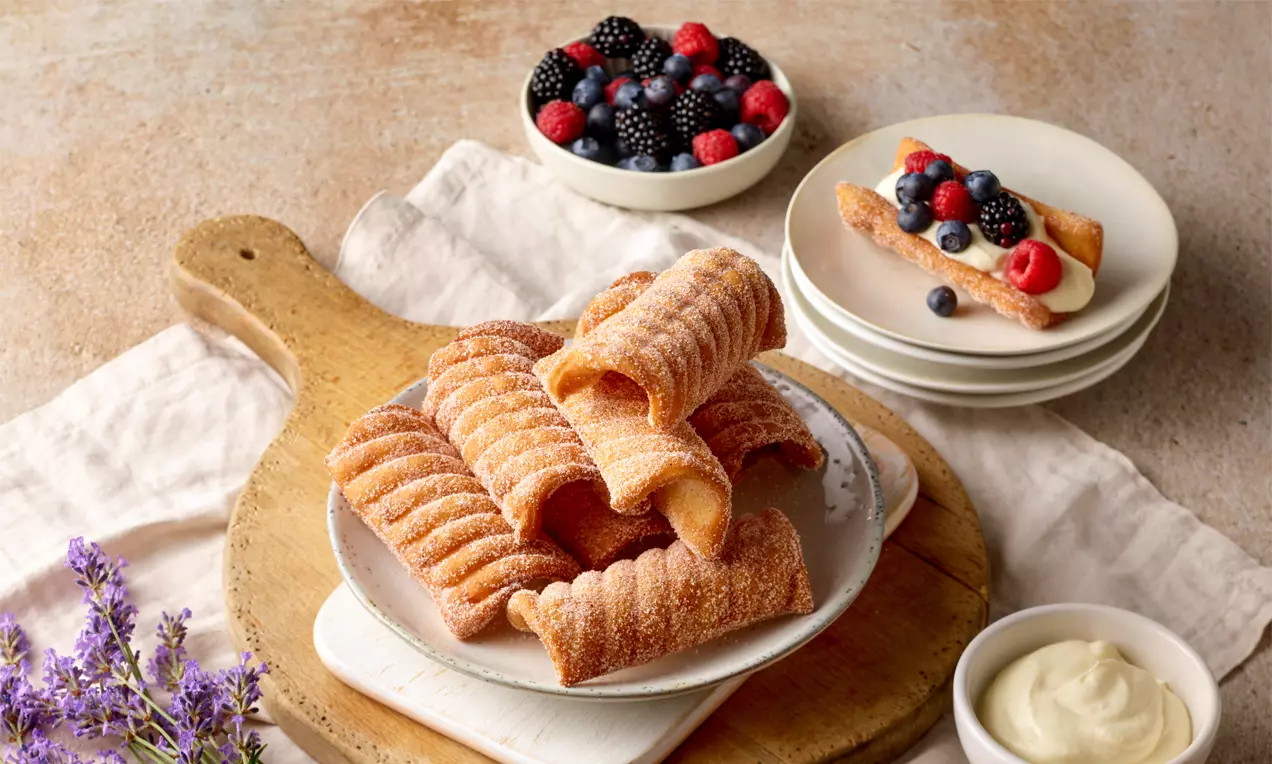 Goldbraune, geriffelte Spagatkrapfen mit feinen Zuckerkristallen auf einem Teller, daneben frische Beeren und cremige Beilage