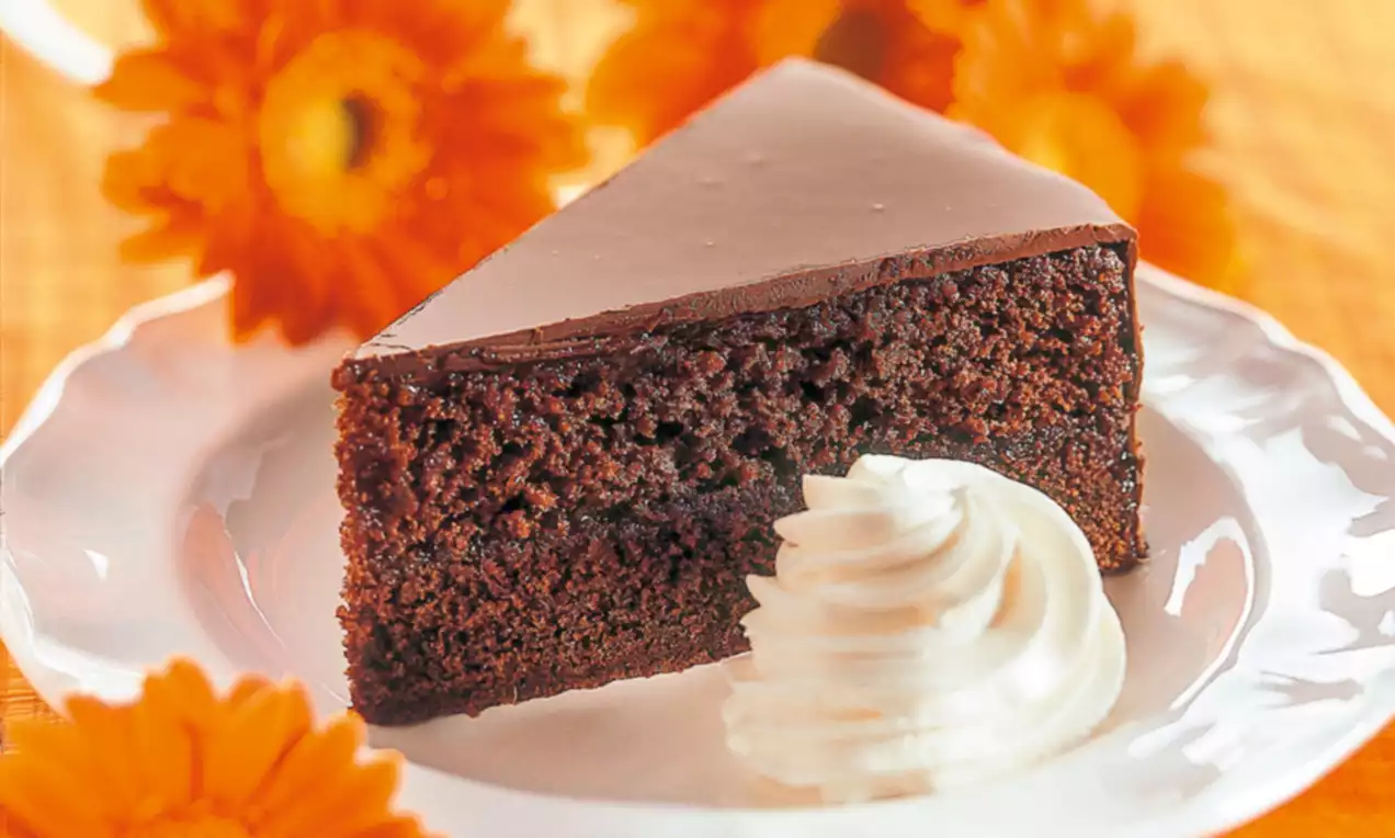 Part de gâteau chocolaté dense et moelleux avec un glaçage brun brillant, servie sur une assiette blanche avec une rosette de crème