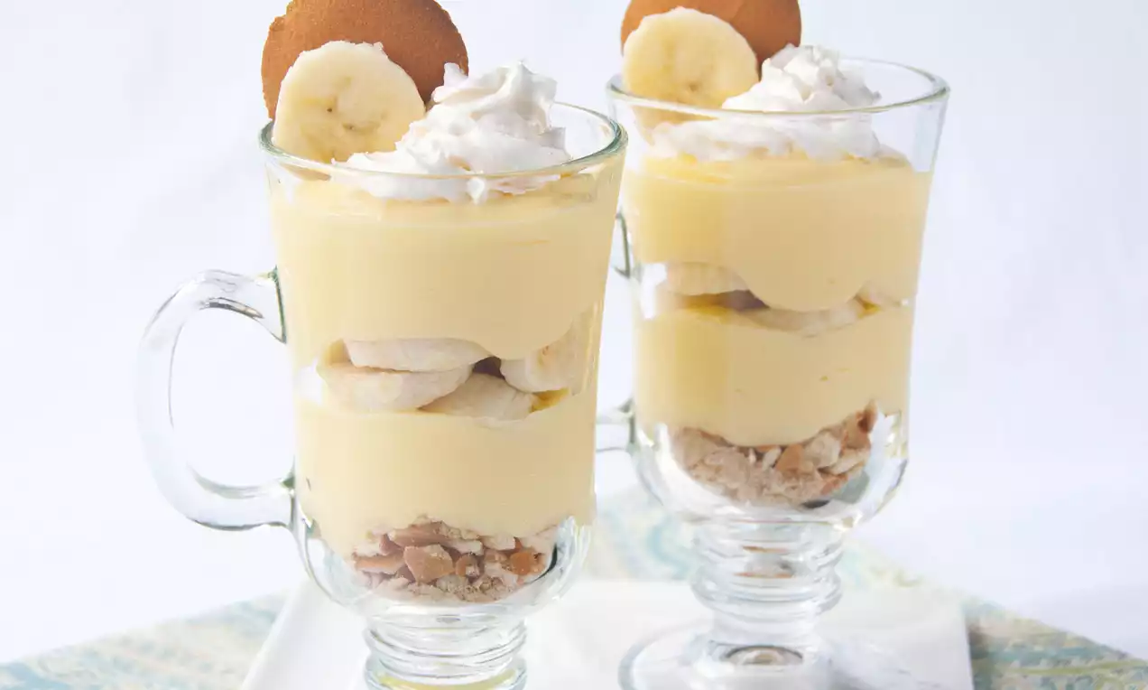 Parfait à la banane en coupe transparente avec couches jaune pâle, tranches de banane, crème fouettée blanche et biscuit doré