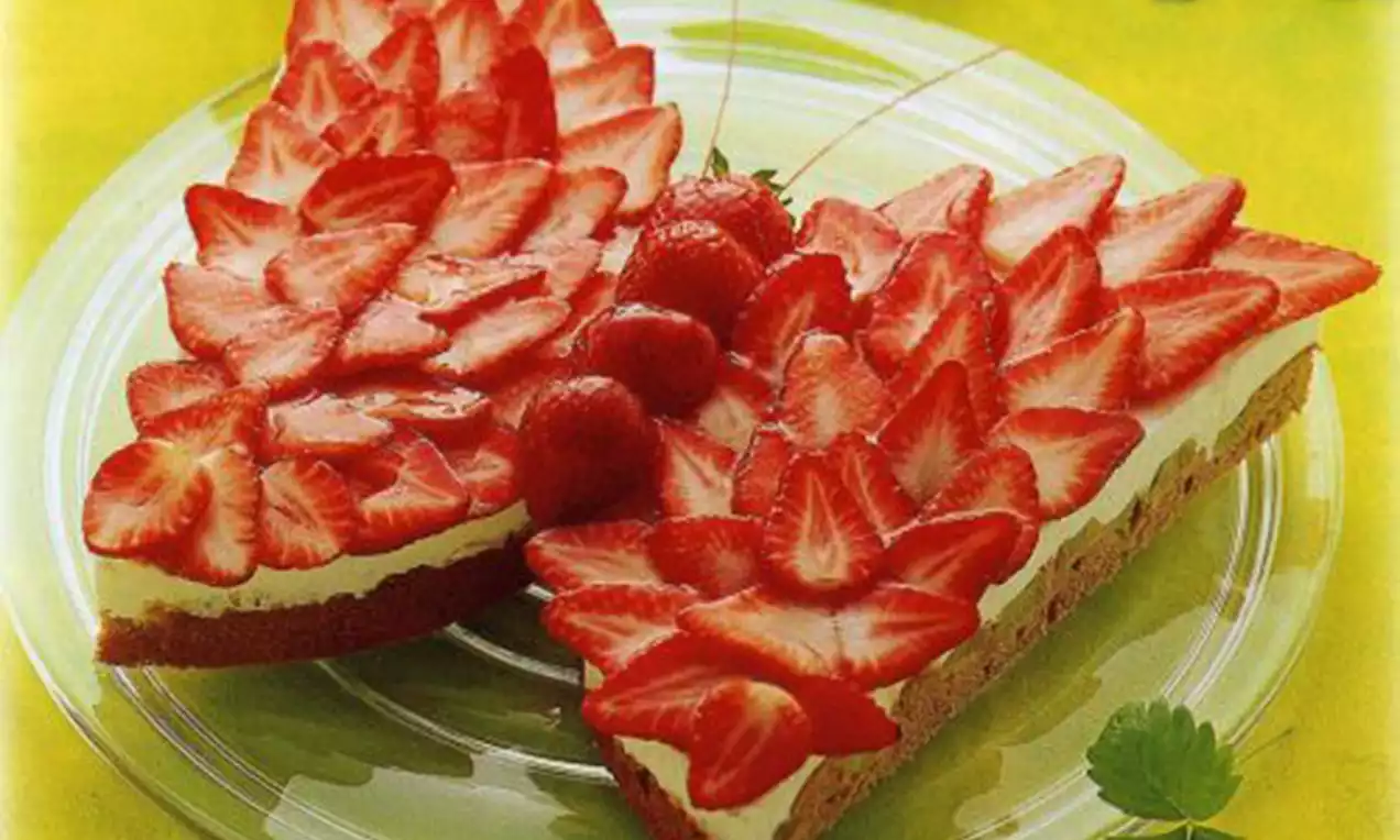 Vlindervormige taart met een lichtbruine bodem, witte roomlaag en felrode aardbeiplakjes, gegarneerd met hele aardbeien op een glazen bord