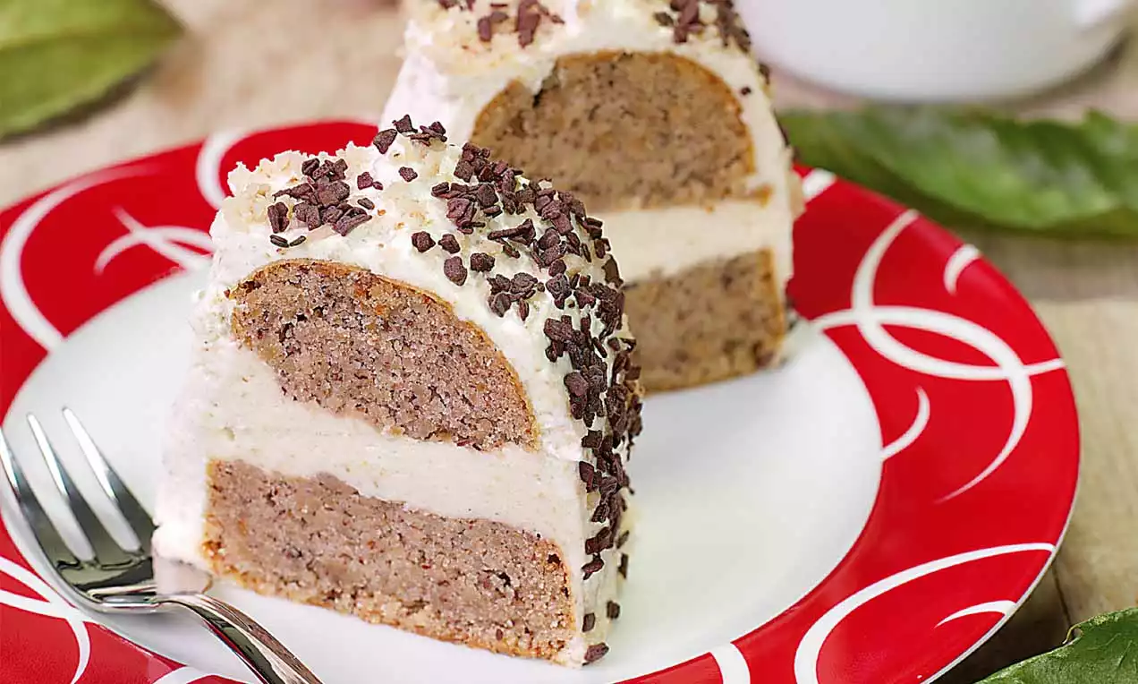 Zwei dreieckige Stücke Kastanienkuchen mit heller Creme, Kastanienboden und Schokostückchen auf rotem Teller mit weißem Muster