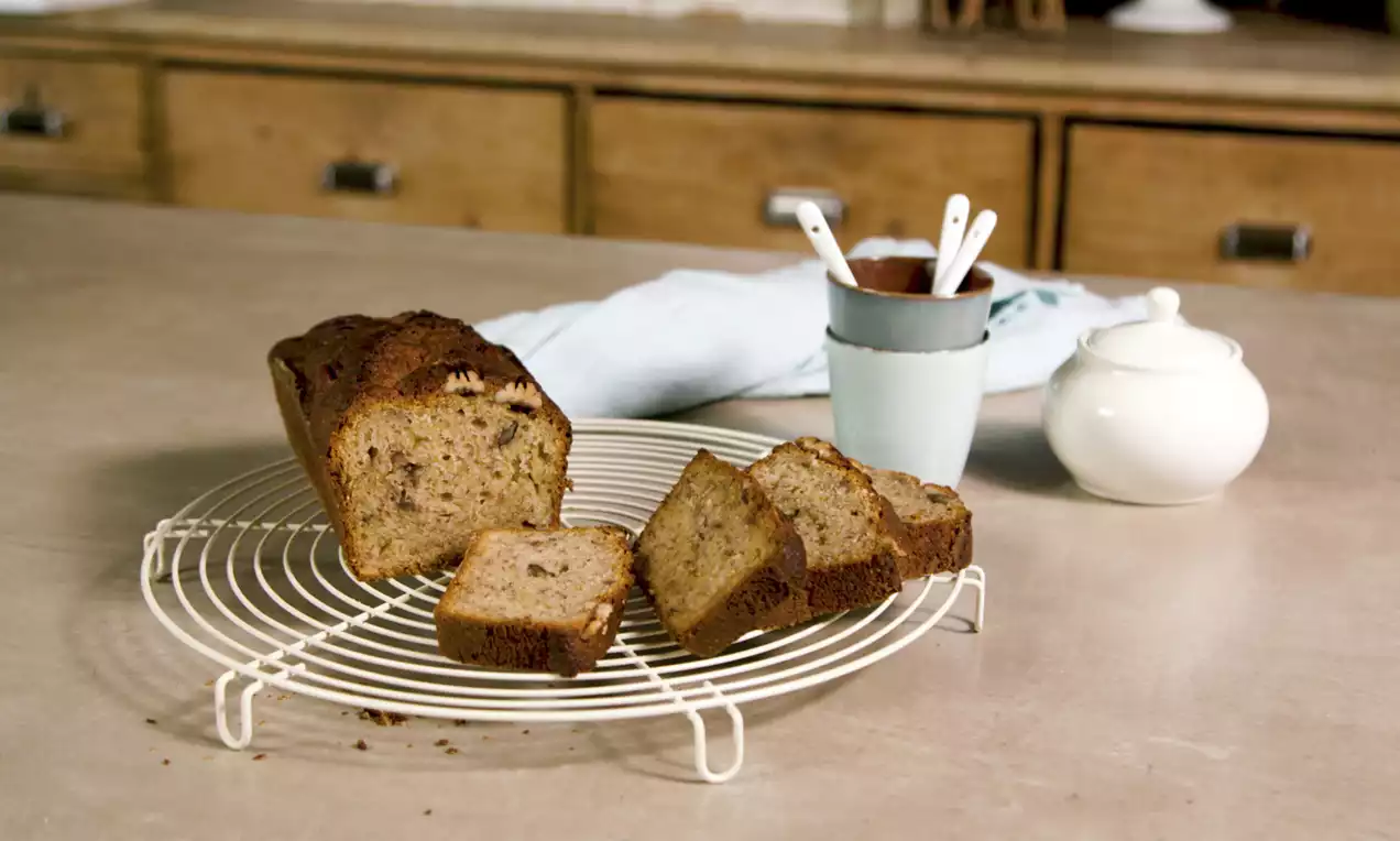 Banenenbrood met grof gesneden nootjes, lichtbruin en luchtig, op een wit metalen rooster met enkele plakjes naast elkaar gelegd